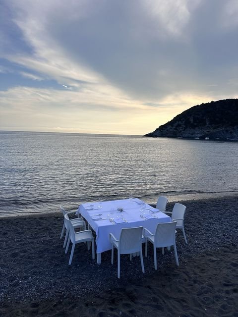 Tavolo per sei sulla spiaggia di sabbia scura, con il mare calmo al tramonto